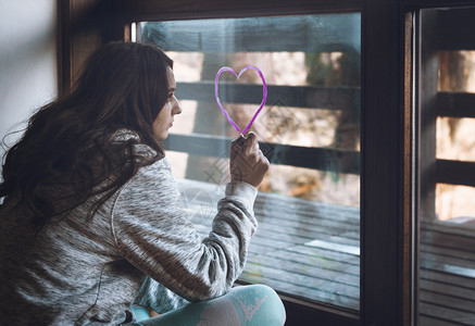 绝望的女人女孩在窗户上画着爱心背景