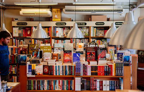 2月12日泰国清迈在小书店里一位欧洲男顾客把各种各样的藏书放在木制书架上上面挂着一盏现代化的大台灯图片