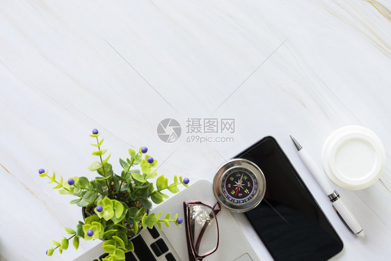 办公桌手机膝上型电脑笔咖啡杯眼镜指南针和植物锅上的办公用具图片