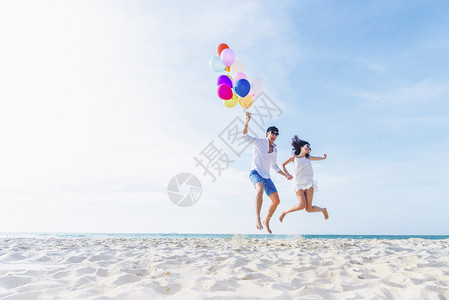 情侣拿着气球在沙滩上跳跃玩耍图片