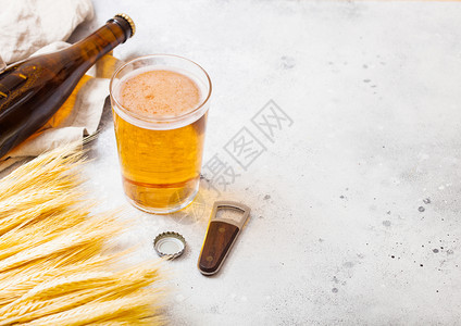 和玻璃瓶的手工艺啤酒生小麦和开瓶器放在石头厨房背景上文本空间顶部视图图片