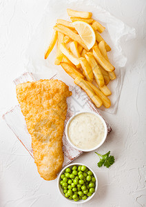 传统英国鱼和薯条在切肉板上加塔酱在白石底有青豆图片