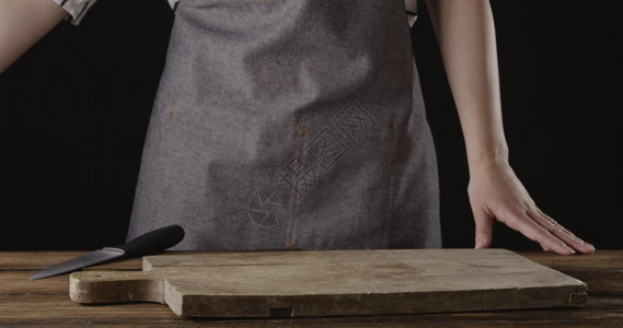 妇女在厨房桌上的刀子木板在黑背景上文本的位置围裙上的厨师站在桌子上黑背景有木板图片