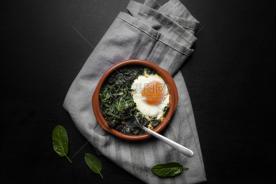 灰色台布背景含菠菜和鸡蛋的黏土锅俯视图图片