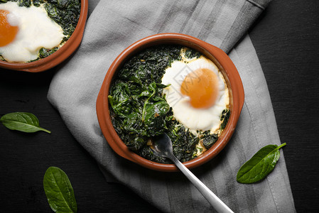 灰色台布背景含菠菜和鸡蛋的黏土锅近视图图片