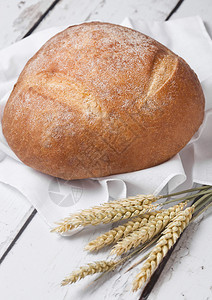 配有厨房毛巾和白木板上小麦的新鲜烤面包图片