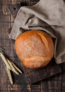 配有厨房毛巾和黑木板上小麦的新鲜面包图片
