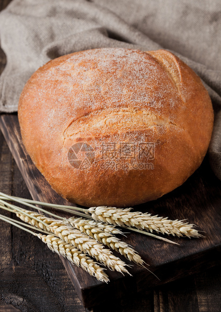 配有厨房毛巾和黑木板上小麦的新鲜面包图片