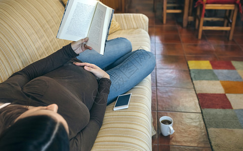 孕妇躺在沙发上读一本书图片