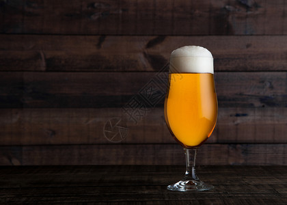 木桌背景上含泡沫的一瓶金啤酒和玻璃杯金啤酒图片