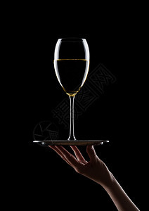 将黑色背景的白葡萄酒杯放在黑色背景上的手持托盘图片
