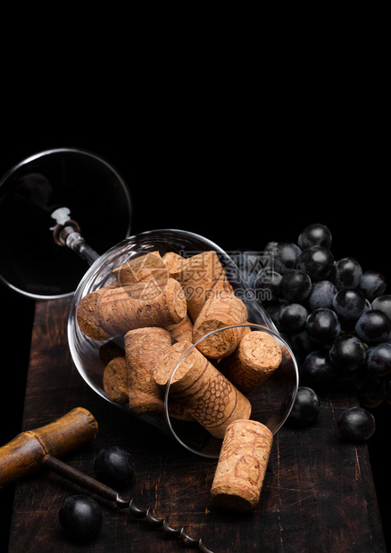 里面装有软塞的葡萄酒杯黑色木板上装有古老的corksew开瓶器和黑葡萄图片