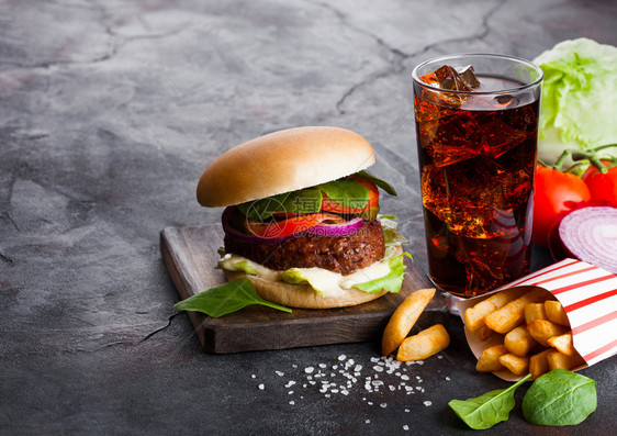 新鲜牛肉汉堡配有酱汁和蔬菜一杯可乐软饮料薯条在石头厨房背景上图片