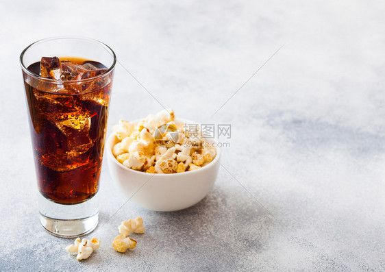 一杯可乐苏打饮料冰块和白碗爆米花零食在石器厨房背景图片