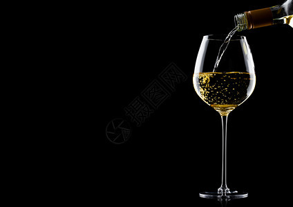 将白葡萄酒从瓶子倒到玻璃在黑色背景上隔绝图片