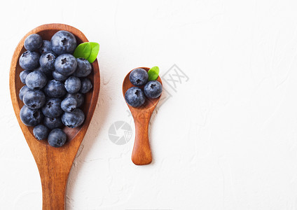 鲜生有机蓝莓叶子在大木勺上小在白色厨房背景上食物概念图片