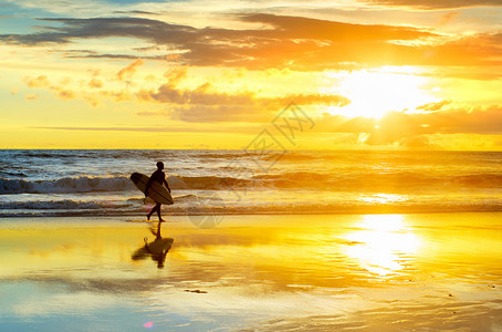冲浪者在沙滩上行走的脚影与冲浪板日落图片