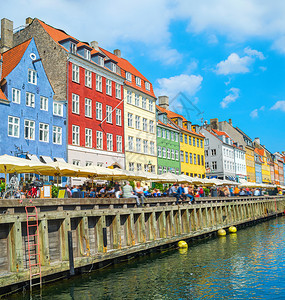 在阳光明媚的日子里在有咖啡馆和餐的Nyhavn河堤岸上旅游的客乘运河面甲根登山的船图片