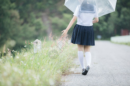 下雨时在自然行走道上带着雨伞行走的亚裔女学生肖像图片