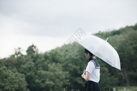 下雨时在自然行走道上带着雨伞行走的亚裔女学生肖像图片