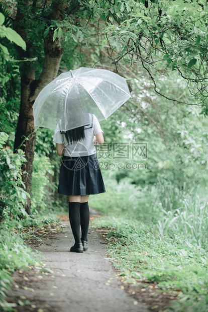 下雨时在自然行走道上带着雨伞行走的亚裔女学生肖像图片