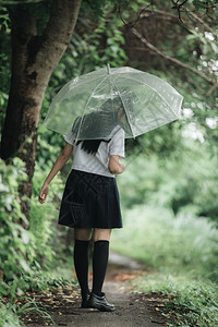 下雨时在自然行走道上带着雨伞行走的亚裔女学生肖像图片