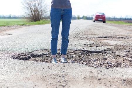 一个女孩站在坏道路的一个洞里图片