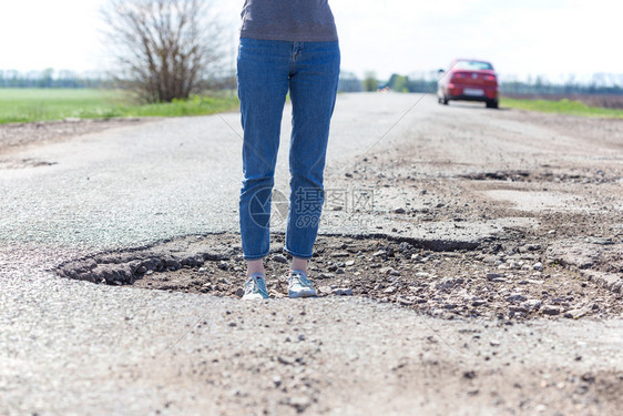 一个女孩站在坏道路的一个洞里图片