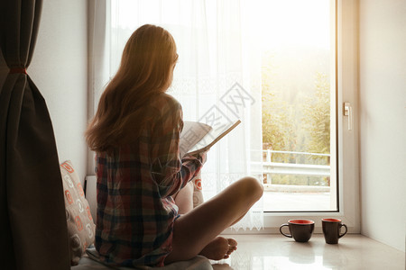 女孩拿着一本书坐在窗台上外有明亮的阳光图片