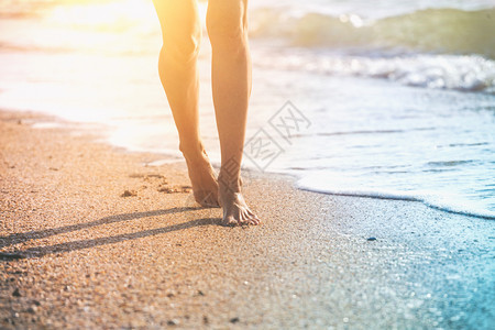 在夏日海滩上沿着水和沙子的潮流行走年轻女子近腿图片