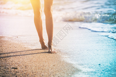 在夏日海滩上沿着水和沙子的潮流行走年轻女子近腿图片