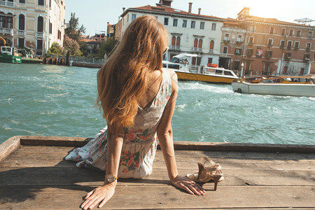 女孩坐在威尼斯运河附近的码头上图片