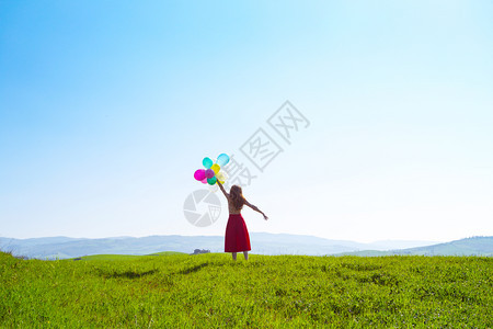 在草地上快乐的女孩带着多彩的气球在蓝天和绿草地上图片
