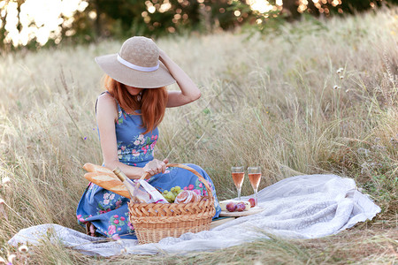 坐在野餐篮子和面包葡萄酒眼镜和卷饼旁边的笑女孩图片