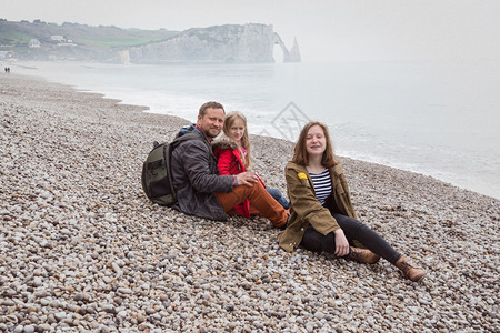 喜笑的爸和两个女儿坐在古典海滩上图片