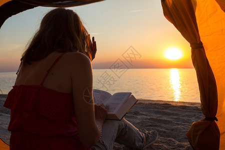 女孩在黎明的海滩上一个帐篷里读书图片