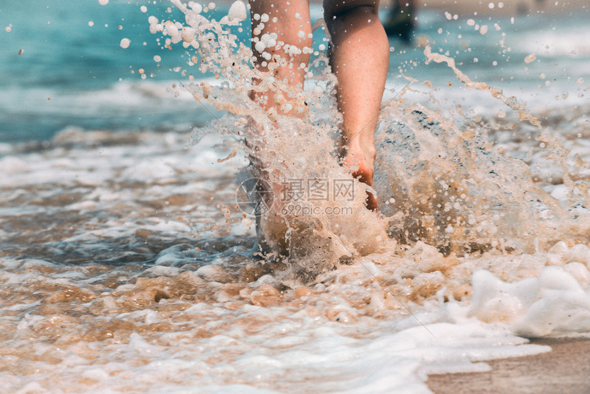 在夏日海滩上沿着水和沙子的潮流行走年轻女子近腿图片