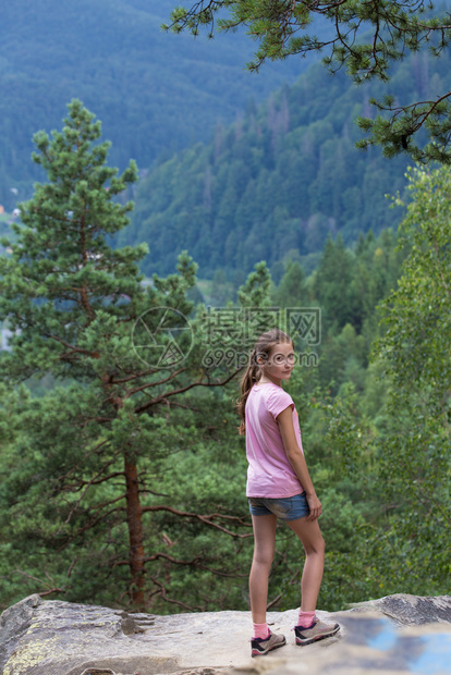 女孩站在岩石悬崖边看着森林山图片