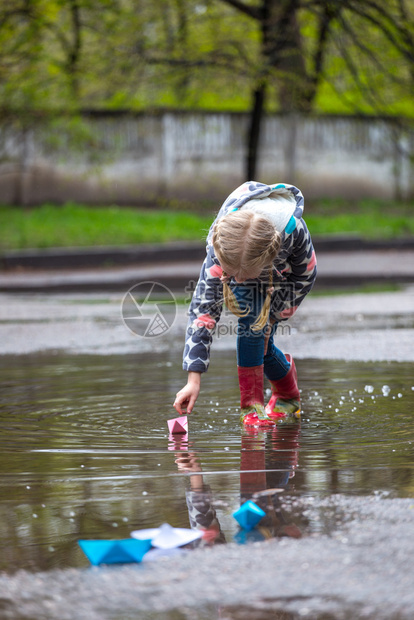 女孩玩着粉红色纸船在雨中的水天漫步图片