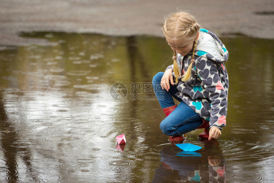 女孩在雨中的水坑里玩纸船图片