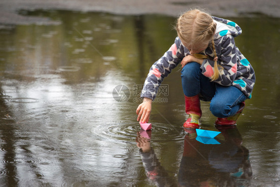 女孩经营粉红色纸船在雨中的水坑里春天图片