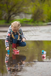 女孩经营粉红色纸船在雨中的水坑里春天图片