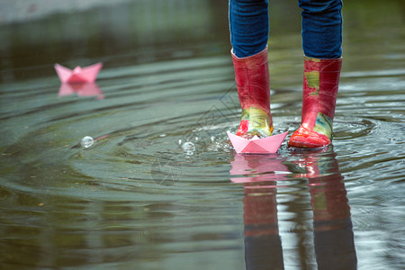 孩子画画红色的雨鞋踩着水坑里玩着纸船背景