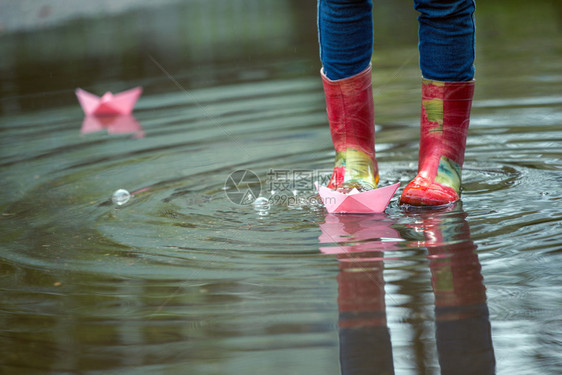 红色的雨鞋踩着水坑里玩着纸船图片