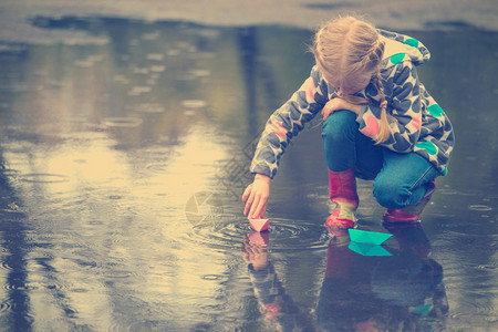 女孩雨中的水坑里玩纸船图片