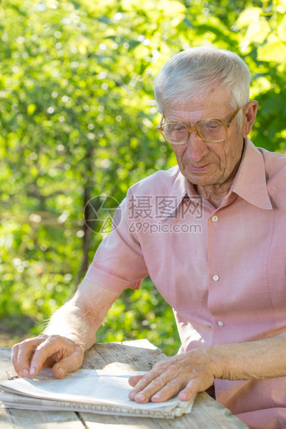 坐在花园桌子上阅读报纸的戴眼镜老人肖像图片