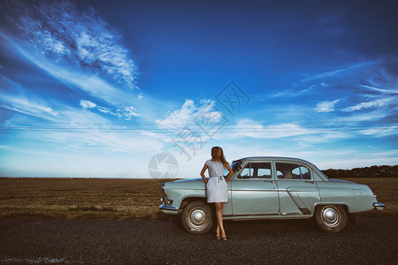 女孩站在一辆旧车背景场和明蓝的天空附近图片