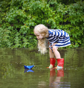 雨天过后带着蓝纸船的女孩在水坑里玩图片