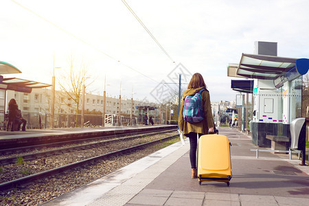 带着背包和黄色大手提箱的游客女孩站在平台上等待火车图片