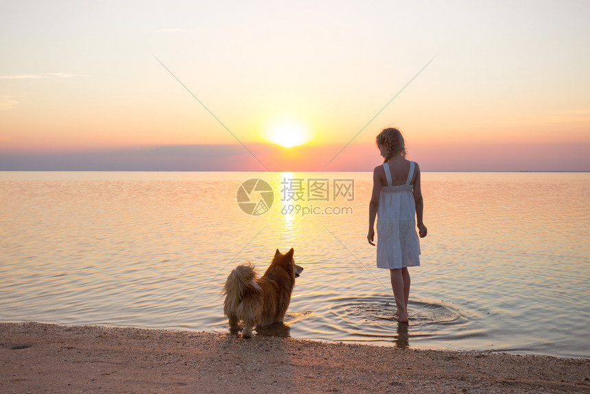 小女孩在日落时正带着一条狗在海边行走图片